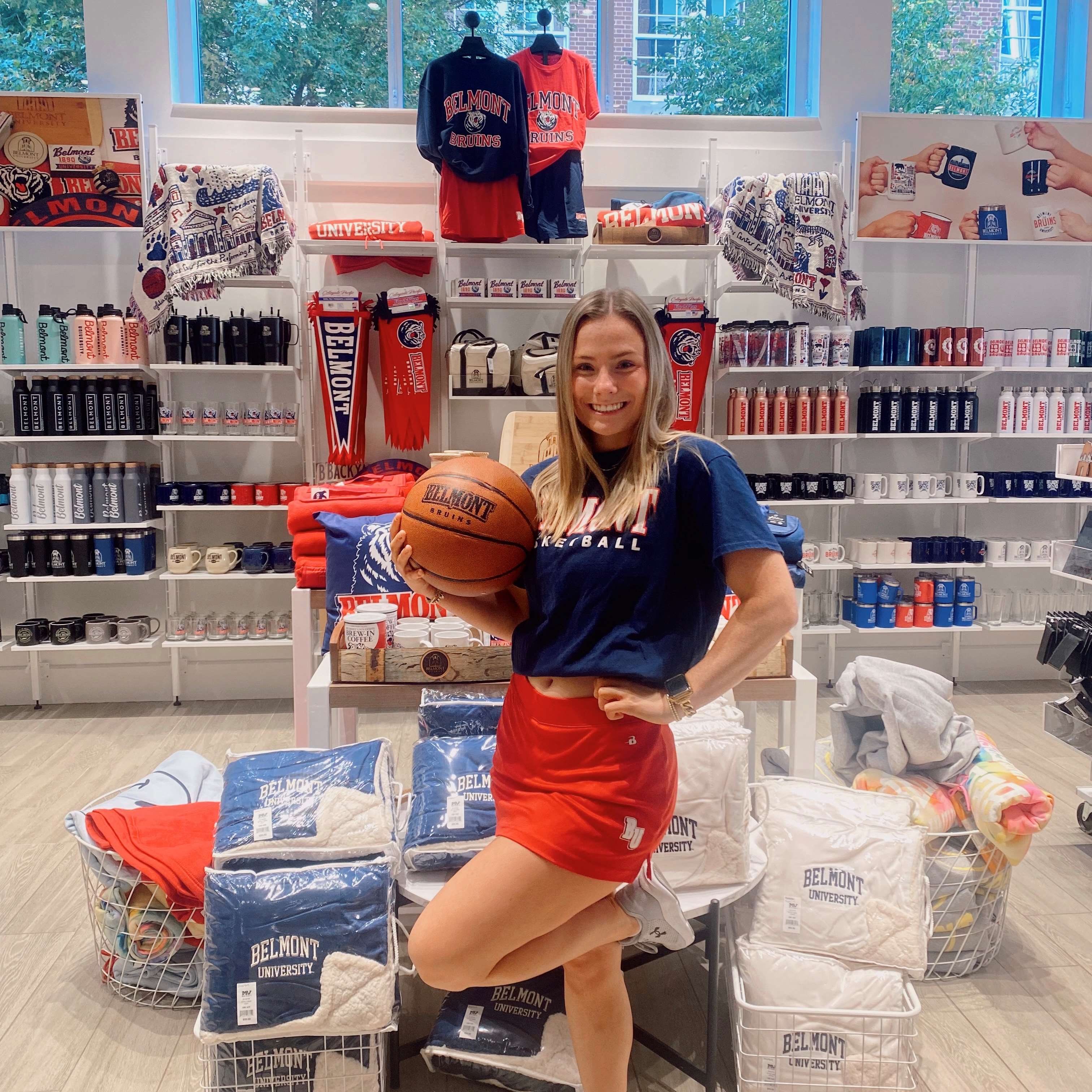 One female Belmont student holding a basketball posing in front of the Mug wall in the BruinShop. Click to view the image on Instagram. 