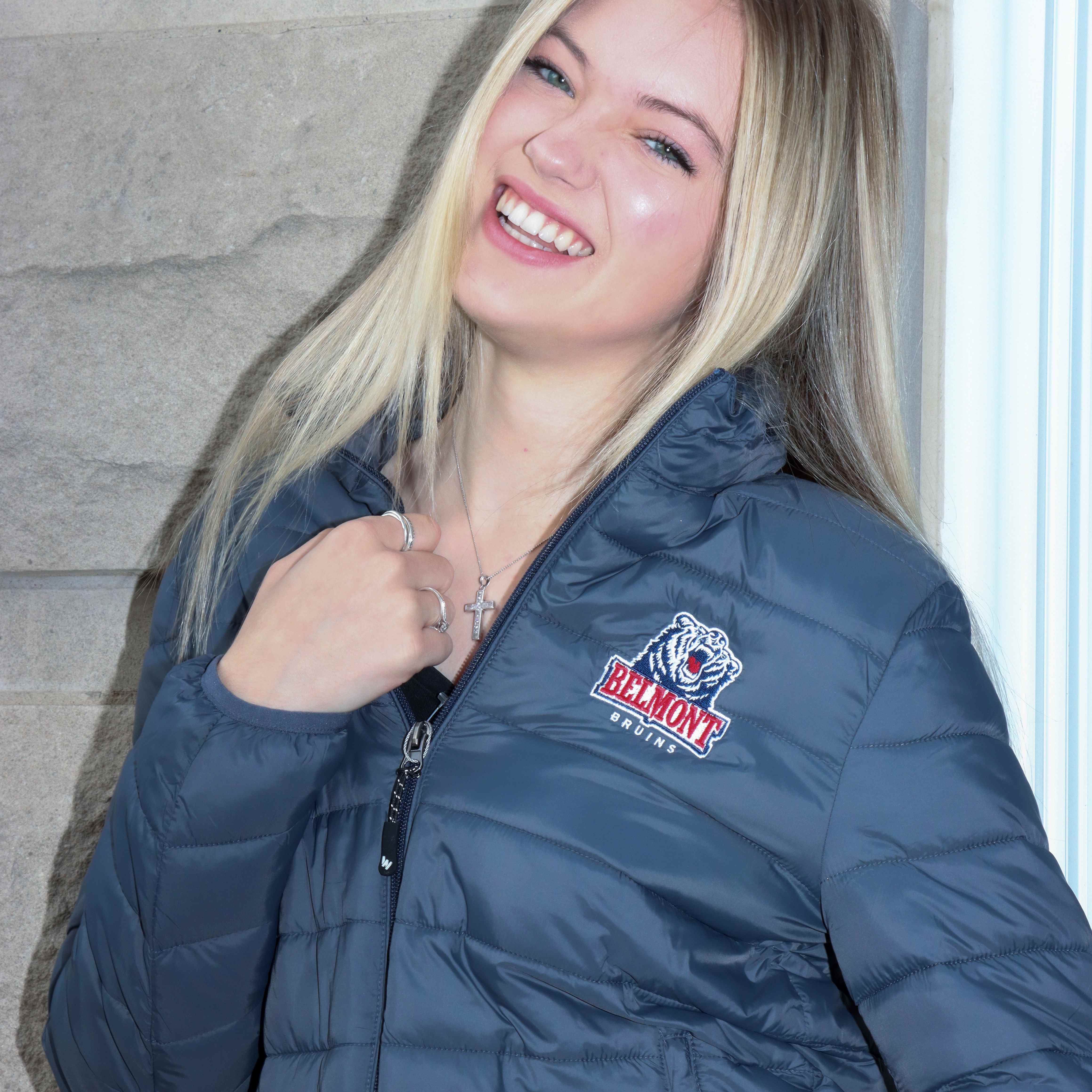 One female Belmont student modeling a grey puffer jacket with the Belmont Bruins logo in the upper left chest. Click here to view video on Instagram.. 