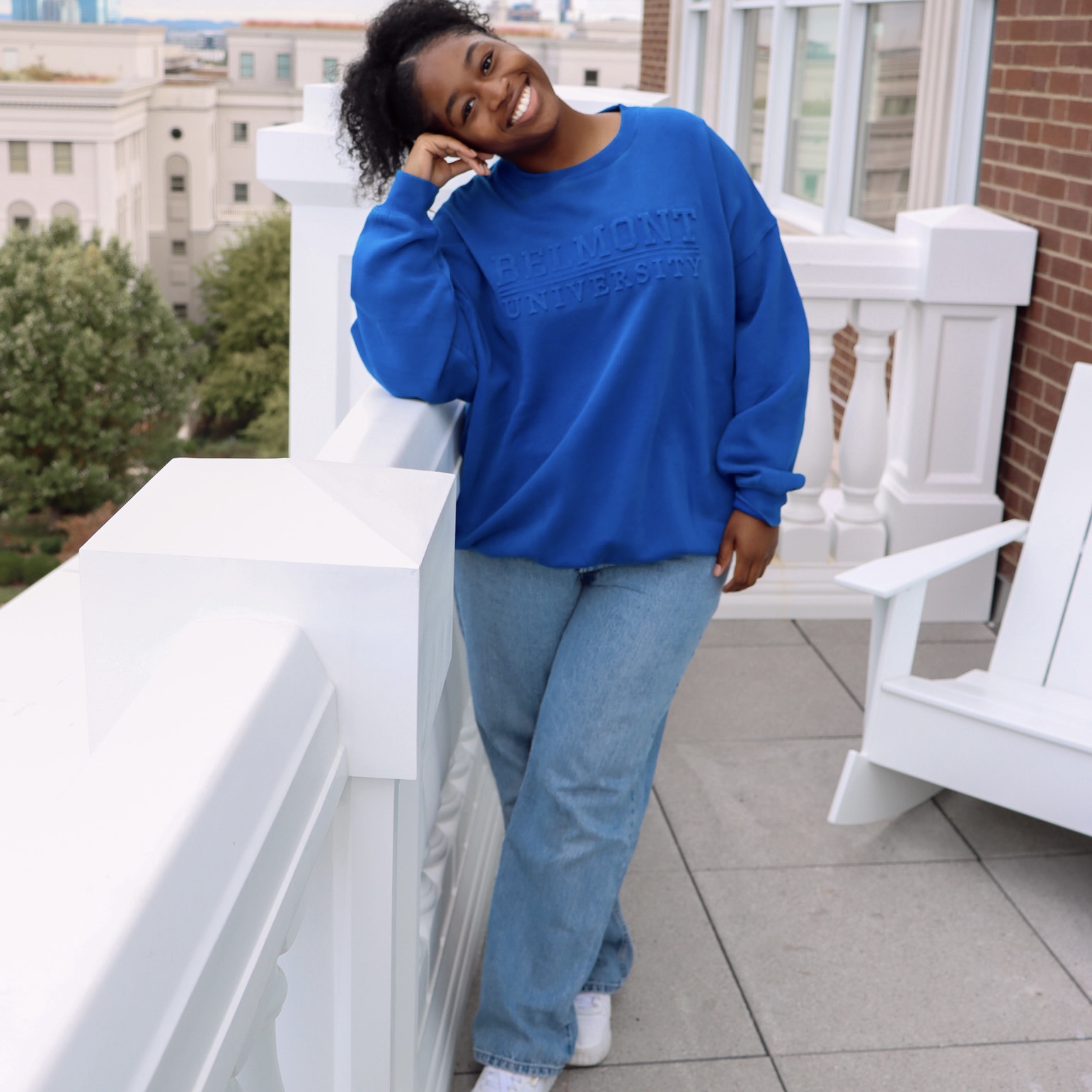 Female Belmont student leaning on a white rail modeling a royal blue Belmont crewneck. Click here to view on Instagram. 