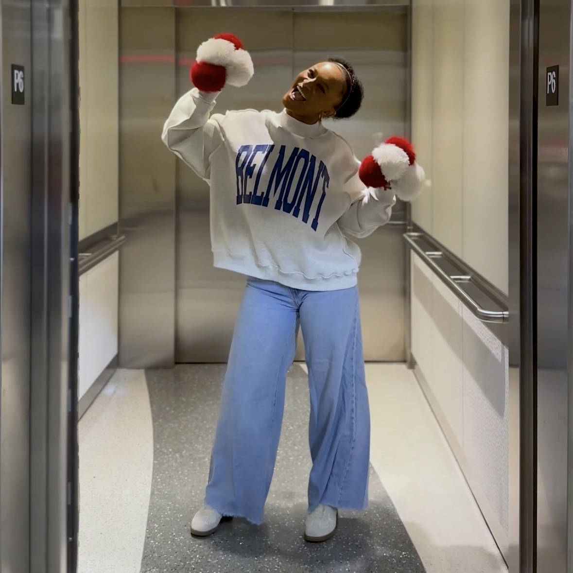 Woman standing in an elevator holding up pom poms and wearing a BruinShop mock neck sweatshirt. Click to view Instagram post